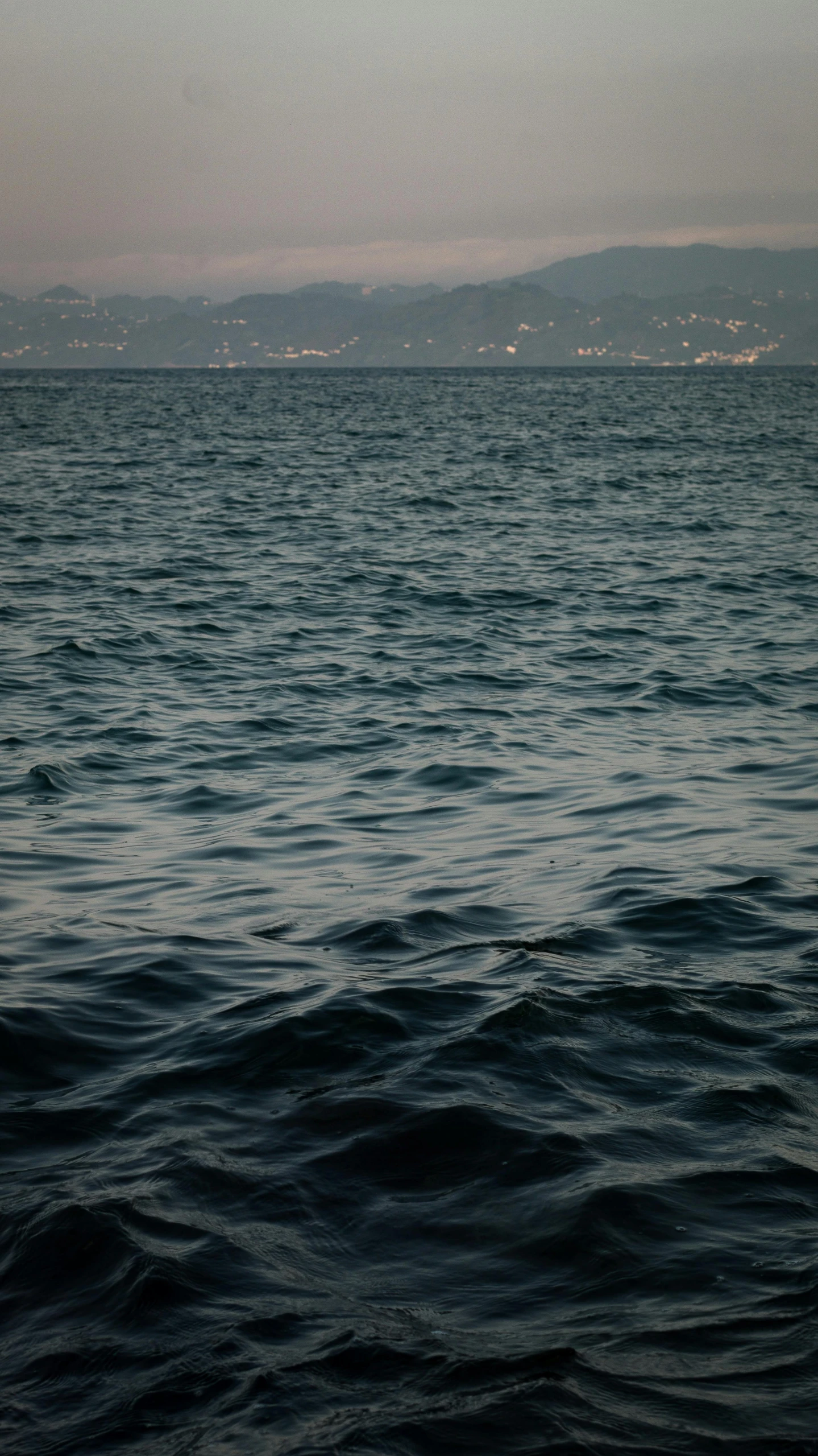 a large body of water with mountains in the distance, an album cover, by Elsa Bleda, unsplash, gulf of naples, dark ocean water, early evening, ocean pattern