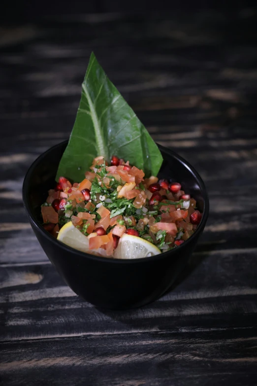 a black bowl filled with food on top of a wooden table, pomegranate, relish, detailed product image, palm