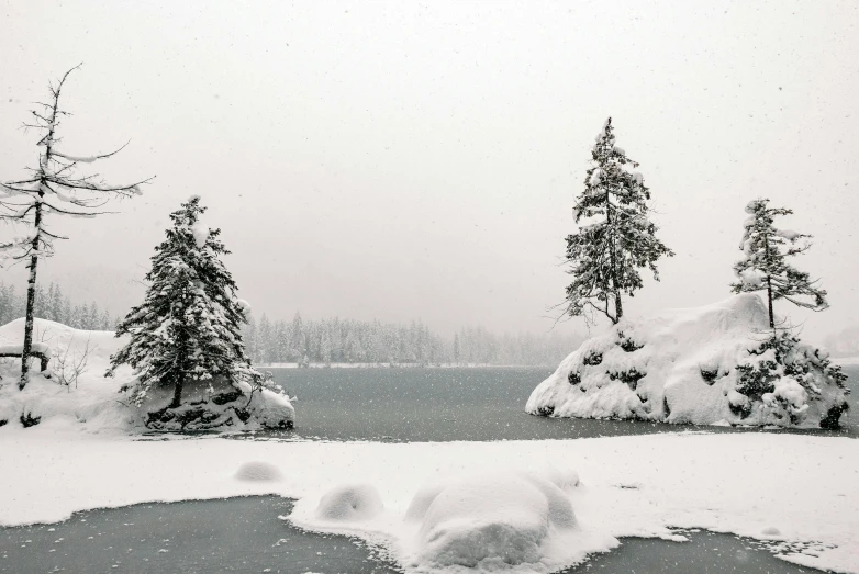 a body of water surrounded by snow covered trees, by Ike no Taiga, pexels contest winner, visual art, two medium sized islands, grey mist, whistler, heavy snow storm