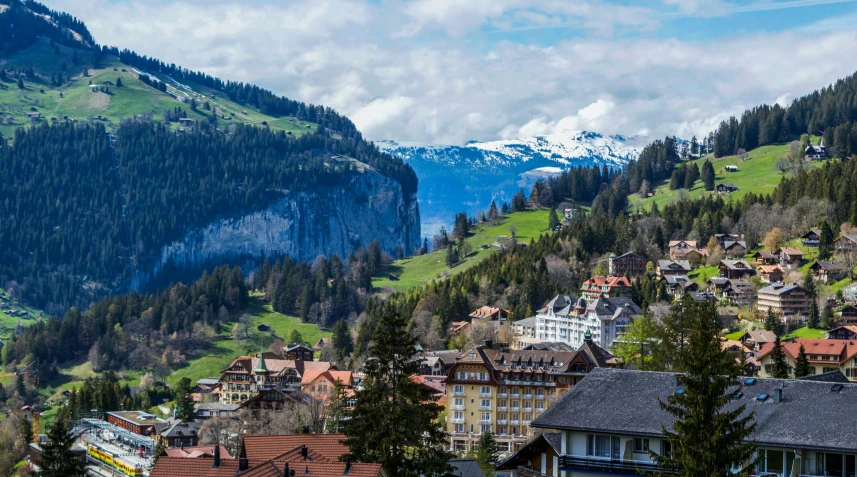a view of a town with mountains in the background, inspired by Karl Stauffer-Bern, pexels contest winner, a green, slide show, trees and cliffs, round-cropped