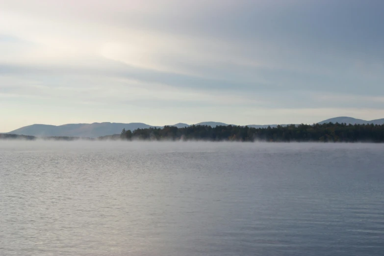 a large body of water with mountains in the background, a picture, inspired by Eero Järnefelt, pexels contest winner, hurufiyya, fog machine, new hampshire, waking up, pale blue fog