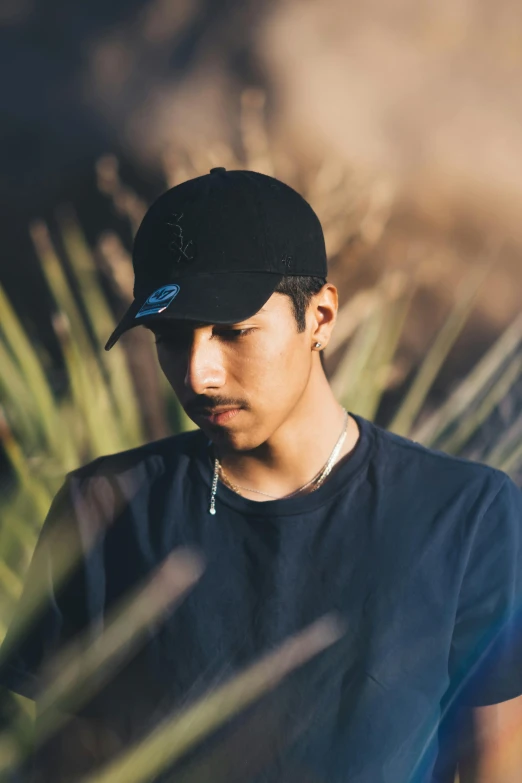 a man looking down at his cell phone, an album cover, unsplash, wearing a baseball cap, portrait of danny gonzalez, profile pose, covered in vines