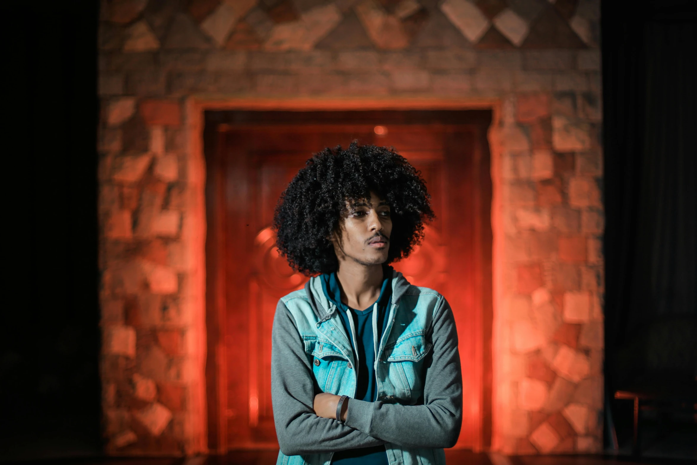 a man standing in front of a red door, an album cover, by Afewerk Tekle, pexels, long afro hair, illuminated, teenage boy, looking serious