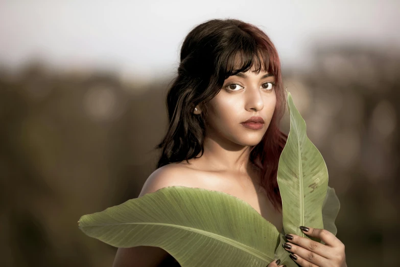 a woman holding a green leaf in front of her face, an album cover, by Max Dauthendey, trending on pexels, renaissance, indian girl with brown skin, with bangs, medium format. soft light, deviantart artstation cgscosiety