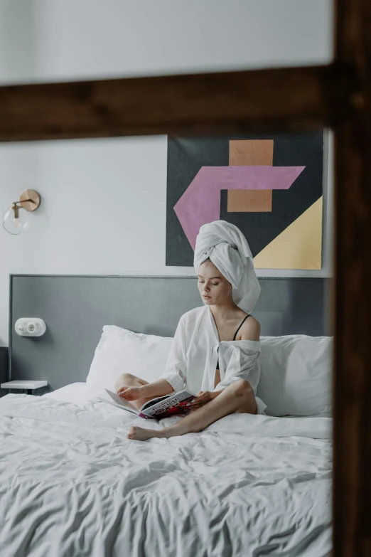 a woman sitting on a bed reading a book, a portrait, by Julia Pishtar, pexels contest winner, wearing a towel, hotel room, turban, gif