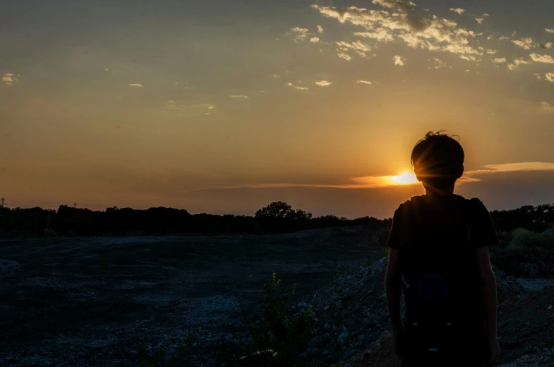a person standing on a dirt road at sunset, looking off into the distance, photo taken in 2 0 2 0, teenage boy, silhouette :7