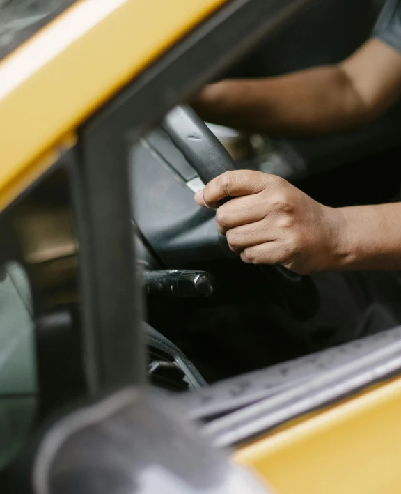 a man sitting in the driver's seat of a yellow car, trending on unsplash, square, non-binary, hand holding cap brim, inspect in inventory image