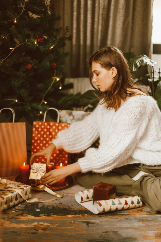 a woman sitting on the floor next to a christmas tree, pexels contest winner, happening, wearing a white sweater, presenting wares, profile image, gif