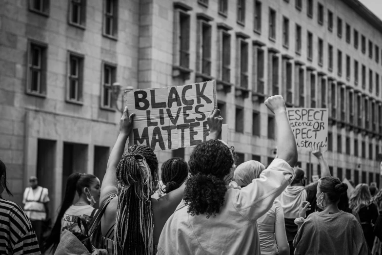a group of people holding signs in front of a building, by Matija Jama, pexels, black arts movement, background image, black black black woman, back and white, justice
