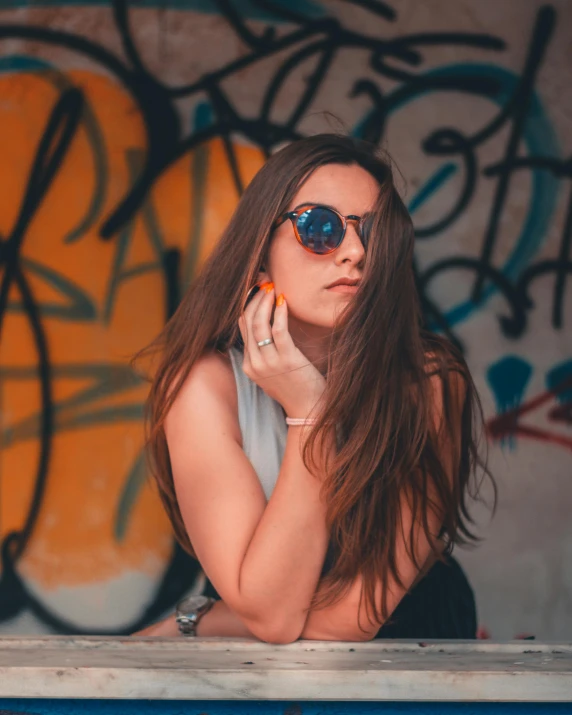 a woman talking on a cell phone in front of a graffiti covered wall, inspired by Elsa Bleda, trending on pexels, sunglasses on, colorful]”, girl with brown hair, low quality photo