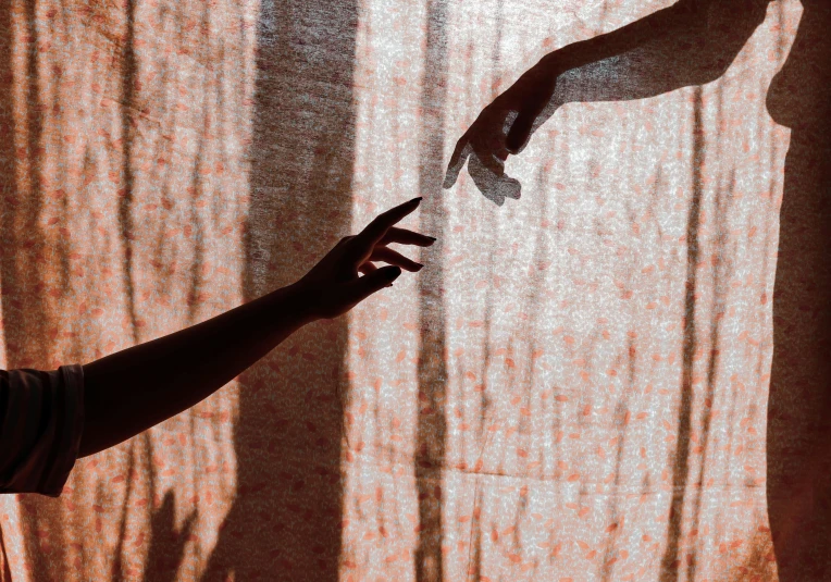 a person holding a piece of paper in front of a curtain, by Lucia Peka, trending on pexels, visual art, two arms that have sharp claws, reaching out to each other, long shadow, two women