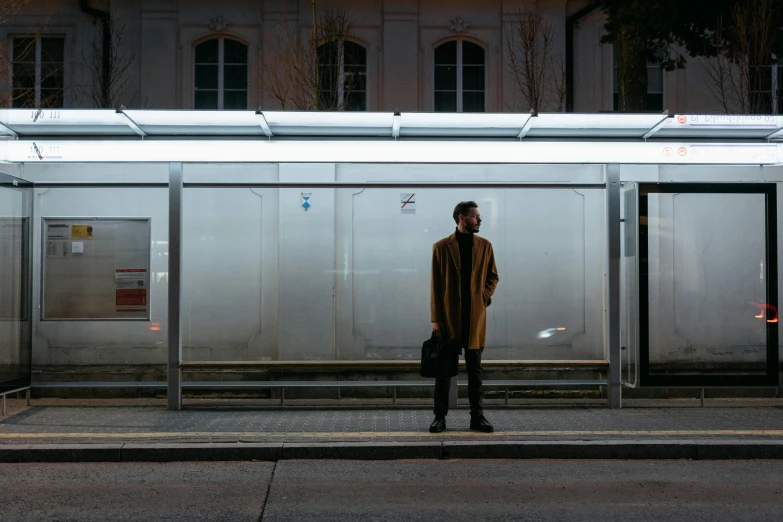 a man standing in front of a bus stop, by Niko Henrichon, pexels contest winner, olafur eliasson, technology cloak, brown, ignant