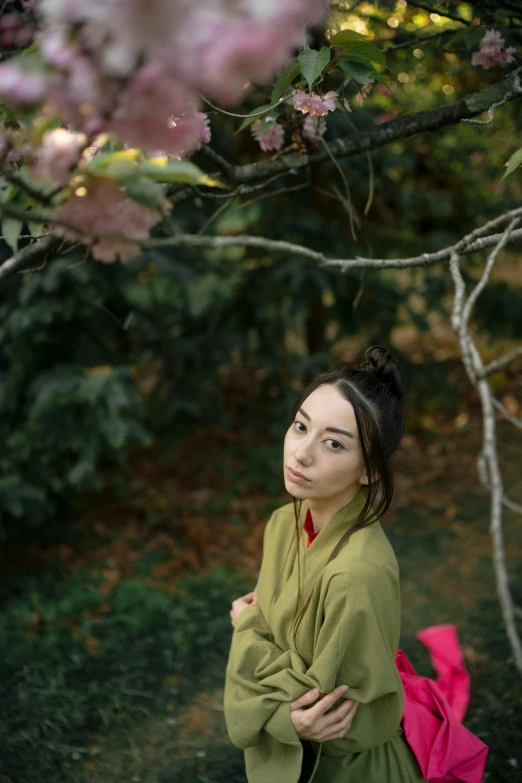 a woman standing under a tree with pink flowers, inspired by Otake Chikuha, unsplash, shin hanga, dressed in a green robe, looking serious, photo of young woman, ethnicity : japanese