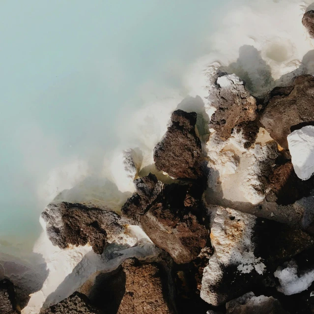 a group of rocks sitting next to a body of water, an album cover, trending on unsplash, white lava, reykjavik, ((rocks)), sulfur