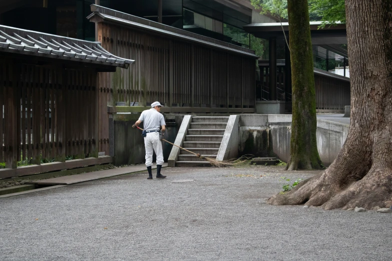 a man standing next to a tree in front of a building, inspired by Sesshū Tōyō, unsplash, shin hanga, sweeping, wooden platforms, maintenance photo