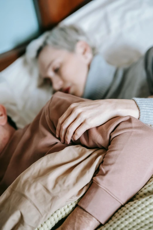 a woman laying on top of a bed next to a man, trending on pexels, comforting and familiar, older woman, lesbian, pale and sickly