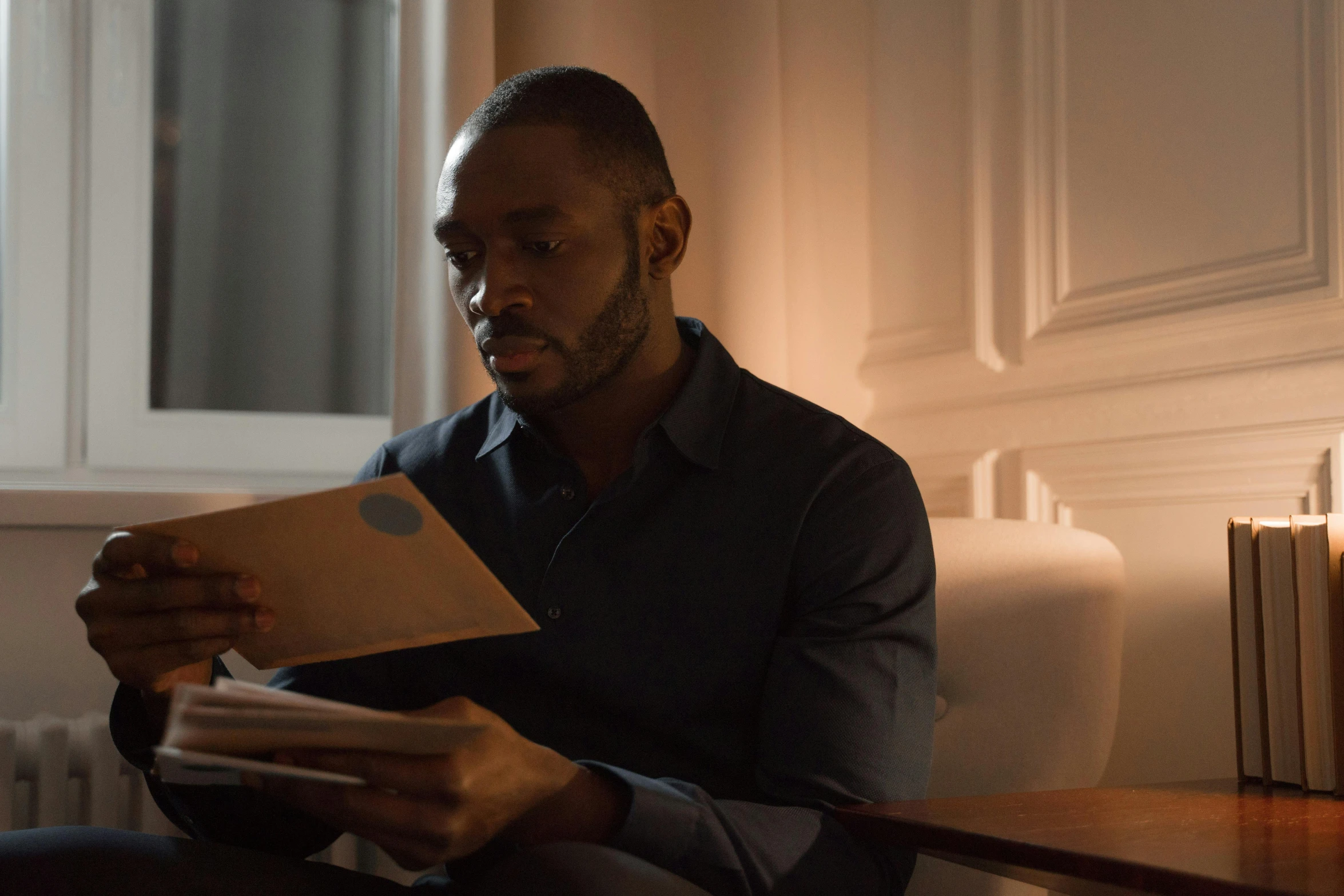 a man sitting on a couch reading a book, pexels contest winner, figuration libre, idris elba as james bond, the lighting is dark, **cinematic, lance reddick