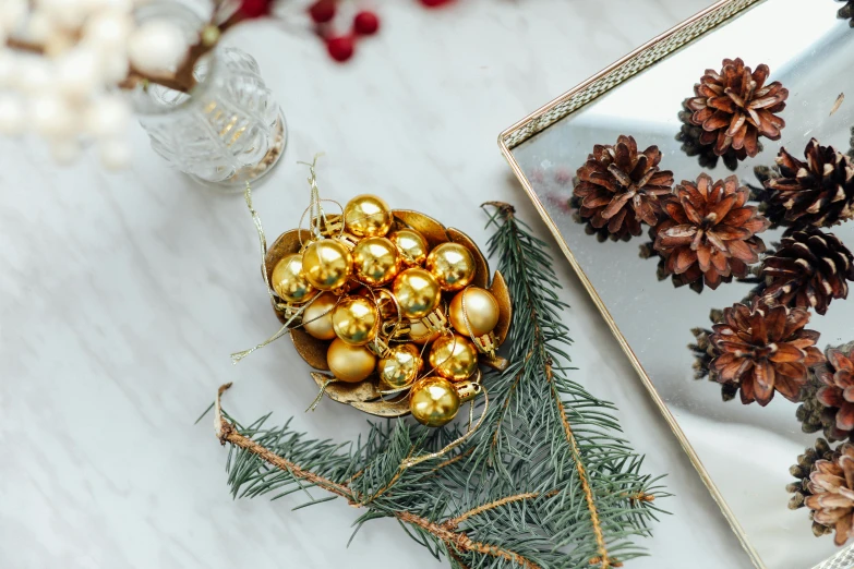 a white table topped with pine cones and ornaments, a still life, trending on pexels, on a reflective gold plate, golden orbs, recipe, golden colour