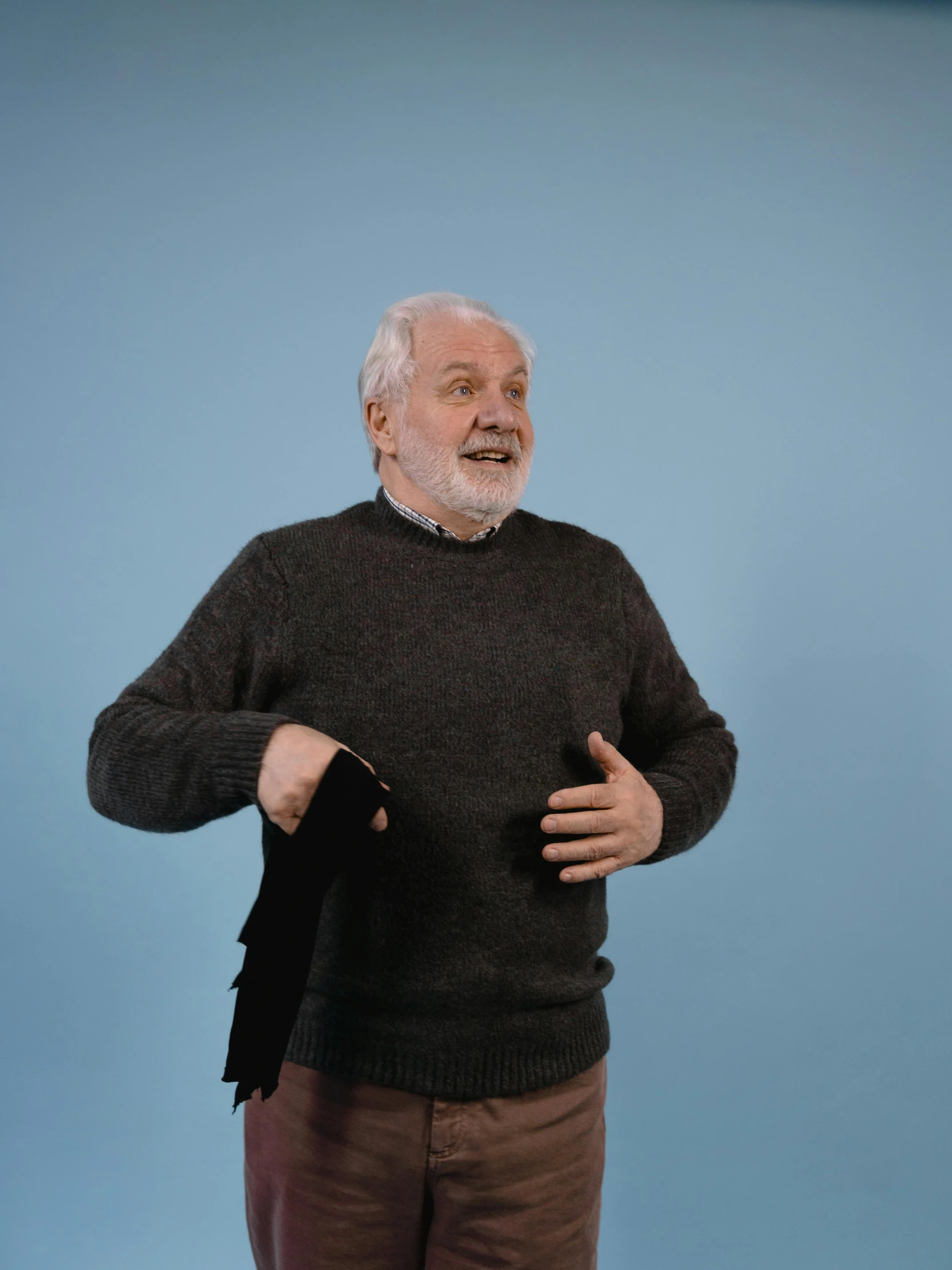 a man standing in front of a blue background, of an old man, wearing a sweater, complaints, standing with a black background