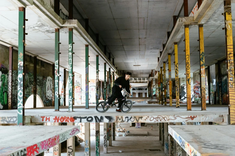 a man riding a bike through a building covered in graffiti, concrete building, vast, ignant, ghost town