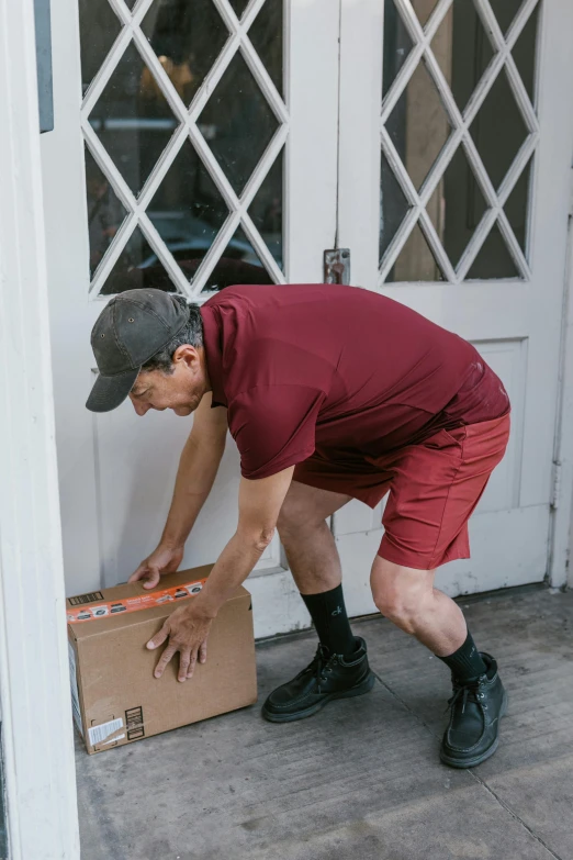 a man holding a box in front of a door, maroon, wearing shorts, stretch, at checkout