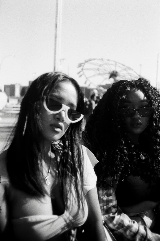 a couple of women sitting next to each other, a black and white photo, unsplash, realism, doja cat, in sun glasses, wavy long black hair and glasses, petra collins