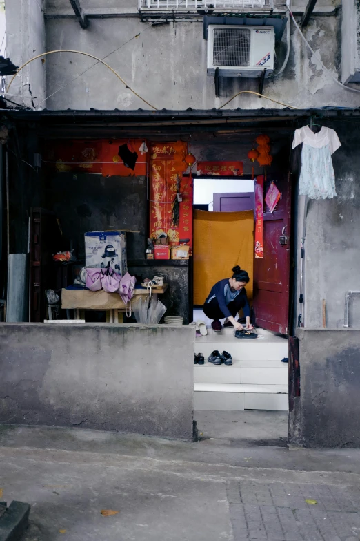 a person sitting on a bench in front of a building, a silk screen, by Shang Xi, pexels contest winner, slum, doorway, sitting on a store shelf, crouching