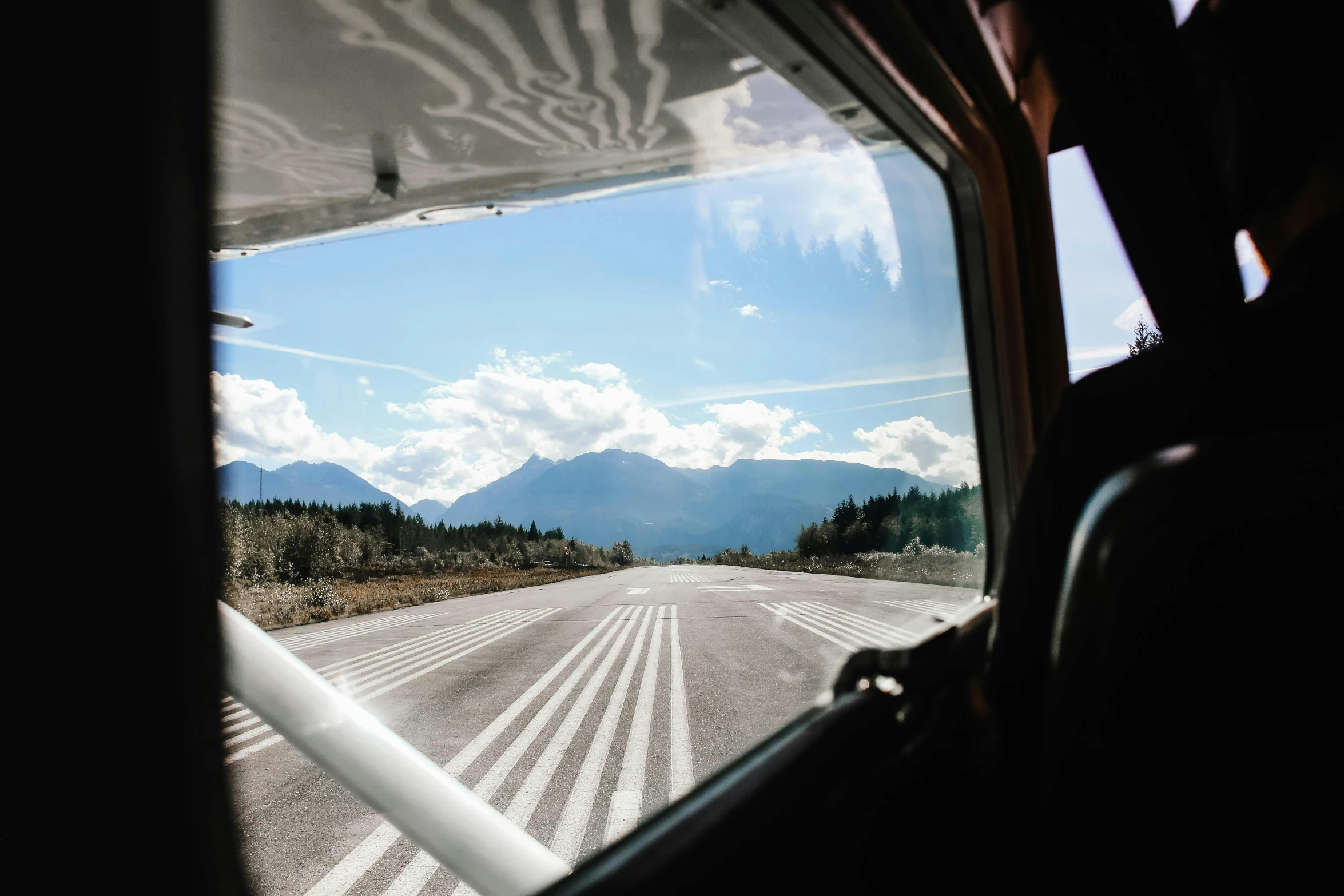 a view out the window of a plane on a runway, by Julia Pishtar, whistler, vw microbus driving, view from inside, with mountains in background