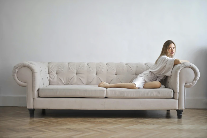 a woman sitting on top of a white couch, inspired by Constantin Hansen, pexels contest winner, arabesque, beige, chesterfield, bed on the right, pale as marble