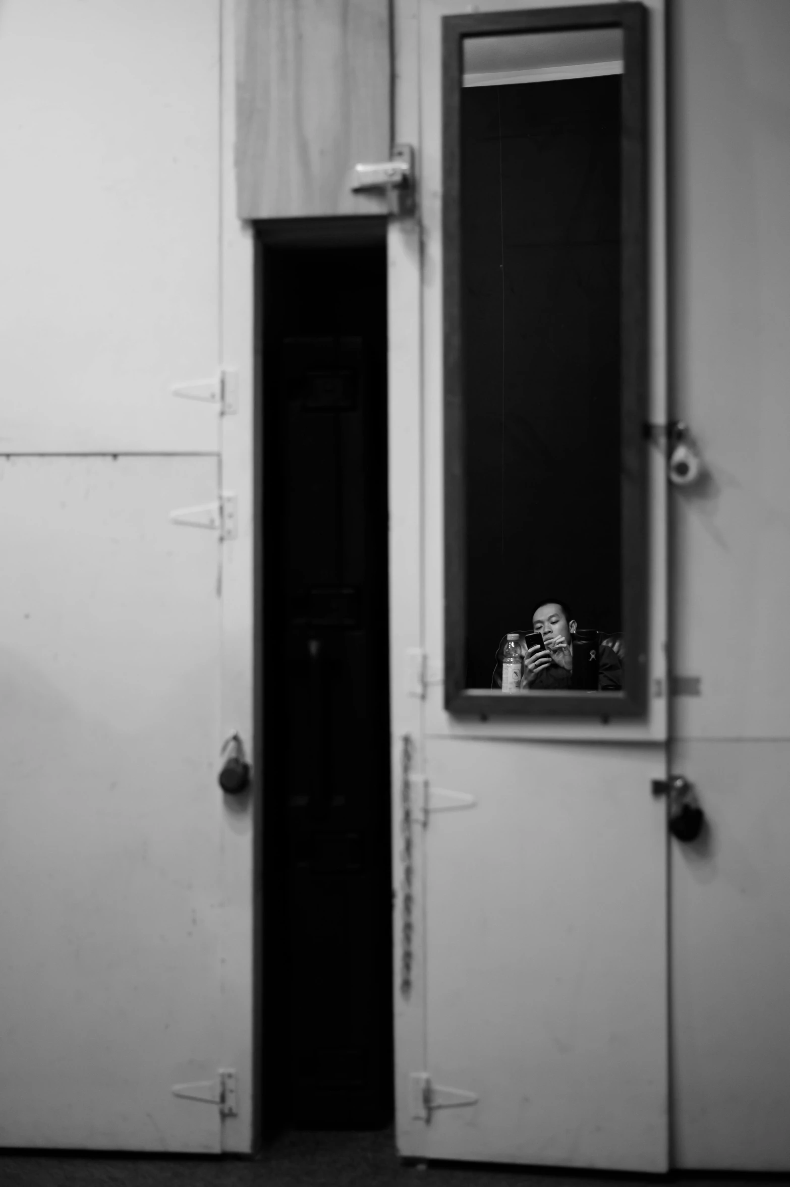 a black and white photo of a door and a mirror, a black and white photo, unsplash, conceptual art, tiny person watching, sitting in a prison, the clown is far from the camera, anna nikonova