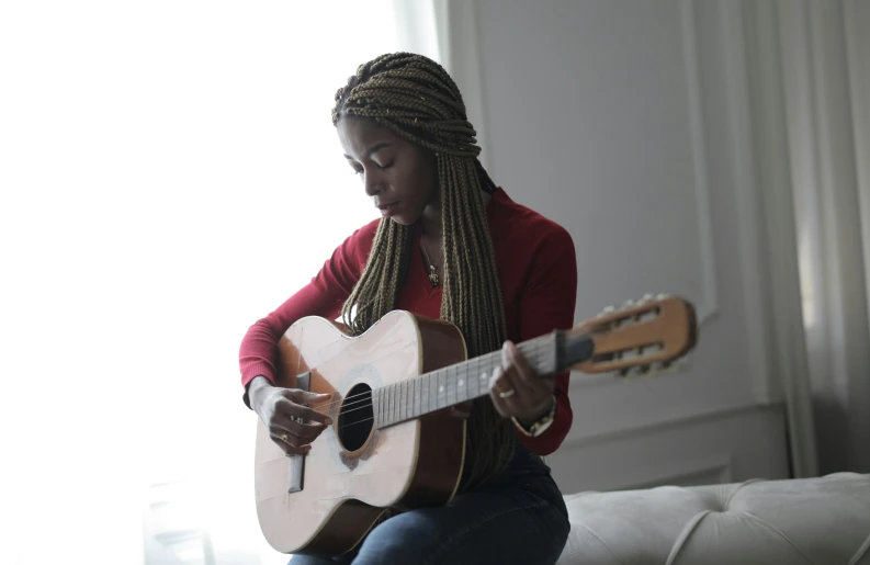 a woman sitting on a couch playing a guitar, by Stokely Webster, pexels contest winner, black arts movement, woman with braided brown hair, instagram picture, ashteroth, slight overcast