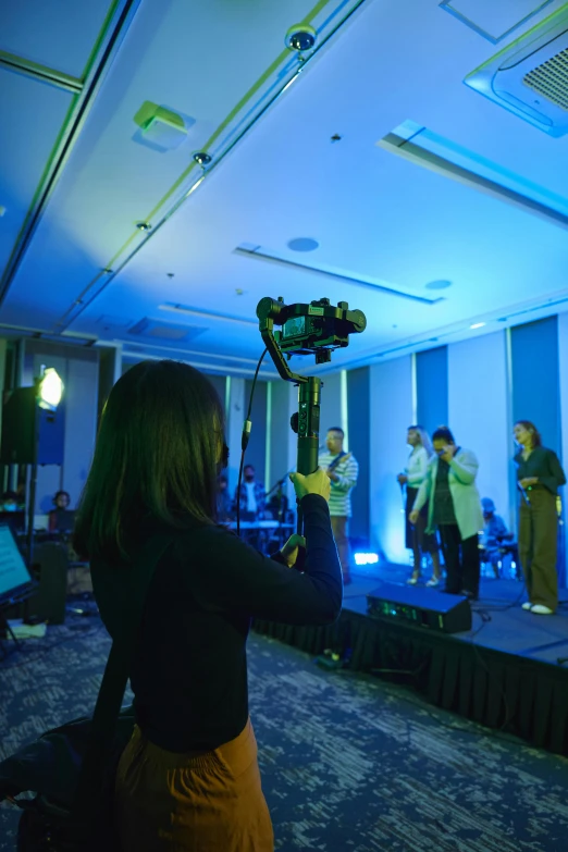 a group of people that are standing in a room, holding a microphone, volumetric underwater lighting, mobile gimball camera, siggraph