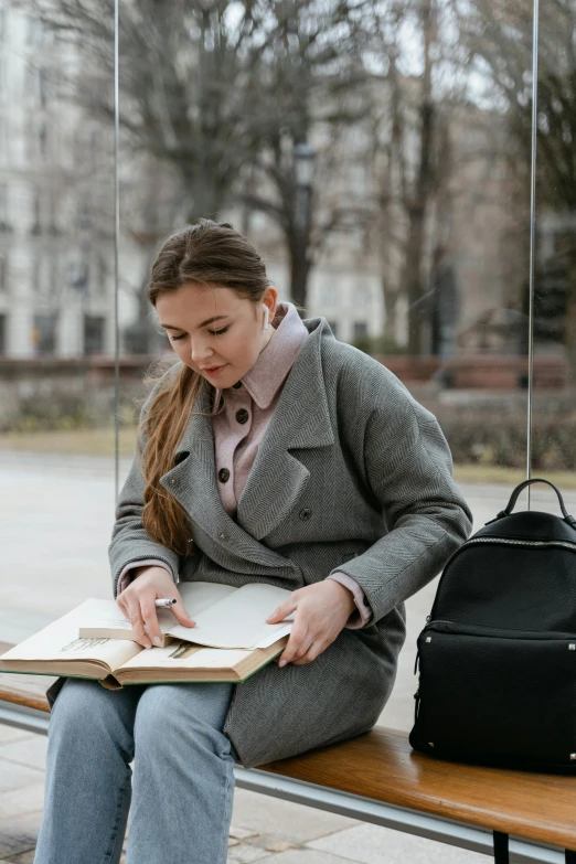 a woman sitting on a bench reading a book, a portrait, trending on pexels, academic art, wearing jacket, grey, textbooks, pastel'