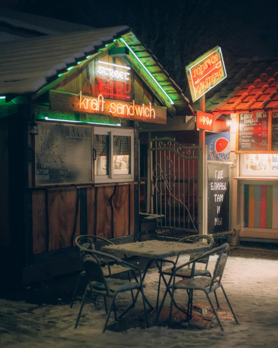 a table and chairs outside of a restaurant at night, by Adam Marczyński, unsplash contest winner, graffiti, snow glow, old shops, convenience store, stood outside a wooden cabin