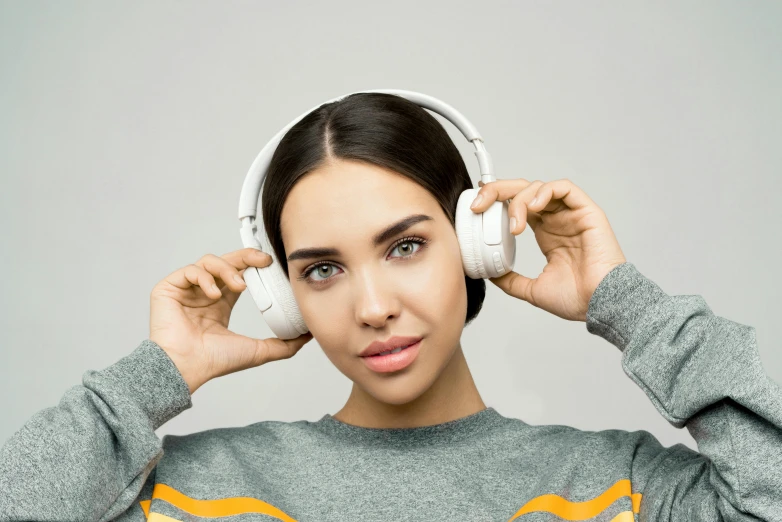 a woman with headphones covering her ears, trending on pexels, on grey background, wearing a white sweater, technological, realistic »