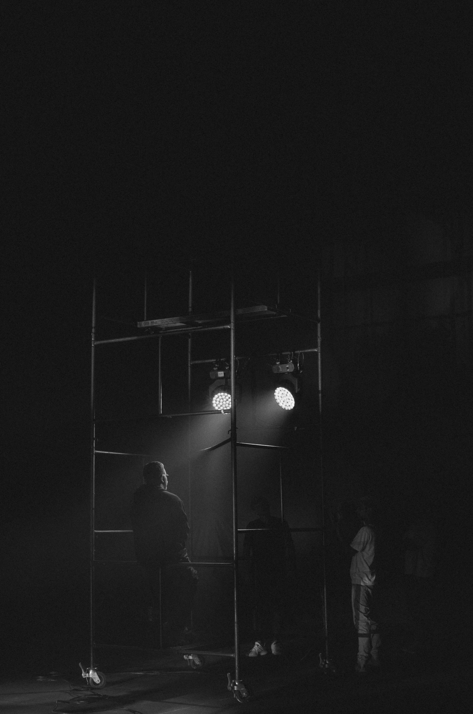 a group of people standing on top of a stage, a black and white photo, by Tamas Galambos, unsplash contest winner, conceptual art, dark. studio lighting, lonely atmosphere, ( ( ( in a dark, busy night