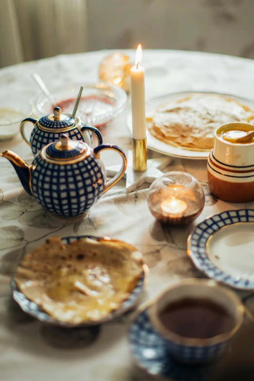 a table topped with plates of food next to a candle, by Alice Mason, unsplash, renaissance, maple syrup, blue and white and gold, teapot, 15081959 21121991 01012000 4k