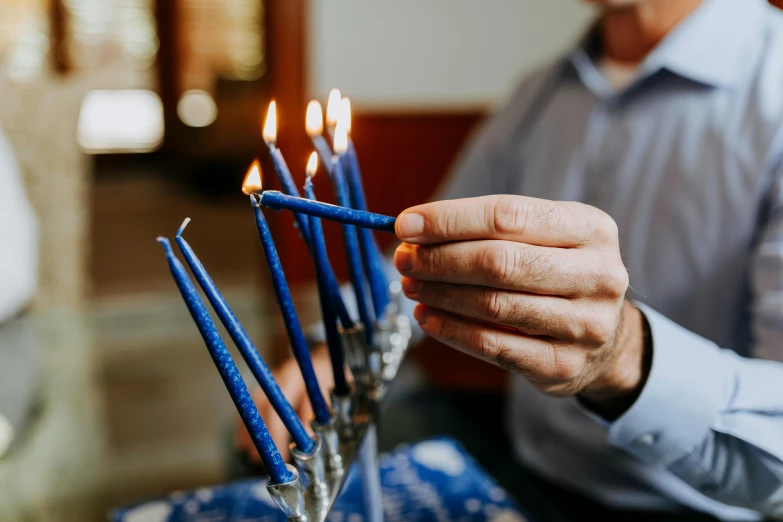 a man lighting a menorah with blue candles, by Julia Pishtar, pexels, instagram post, at home, holding a cane, holiday