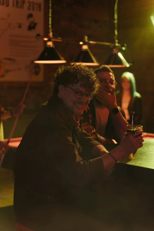 a group of people sitting around a wooden table, dimly lit dive bar, will graham, the poolrooms, ( ( theatrical ) )