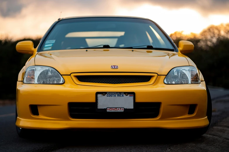 a yellow car parked on the side of the road, inspired by Hiroshi Honda, unsplash, photorealism, perfectly lit face, honda civic, 1999, sundown