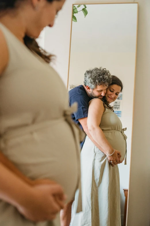 a pregnant woman standing in front of a mirror, by Elizabeth Durack, pexels contest winner, lovely couple, leaning on door, brown, celebrating