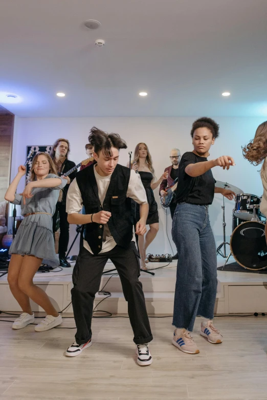 a group of people standing on top of a wooden floor, band playing, other women dancing behind, gen z, ( ( theatrical ) )