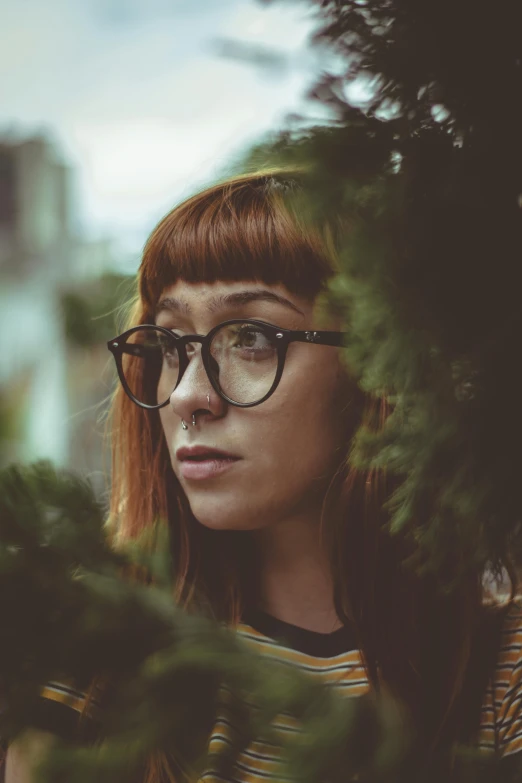 a woman with glasses standing in front of a tree, inspired by Elsa Bleda, pexels contest winner, renaissance, hipster hair fringe, looking through a window frame, square glasses, a redheaded young woman