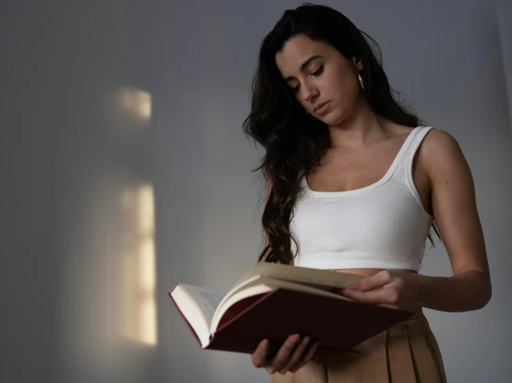 a woman reading a book in a dark room, a character portrait, pexels contest winner, wearing a crop top, in a white room, wearing tank top, wearing a light shirt