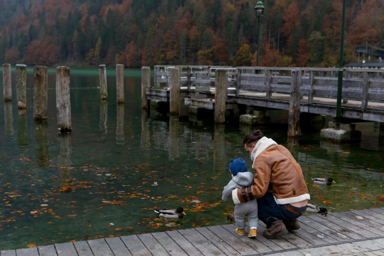 a man and a child sitting on a dock next to a body of water, during autumn, tourist photo, illustration », teals