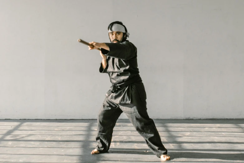 a man in a black outfit holding a baseball bat, inspired by Ma Quan, unsplash, shin hanga, karate pose, wearing a track suit, cardboard, performing