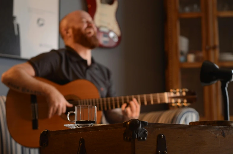 a man playing a guitar in a living room, a portrait, inspired by Jóhannes Geir Jónsson, pexels contest winner, next to a cup, medium head to shoulder shot, performing on stage, wine