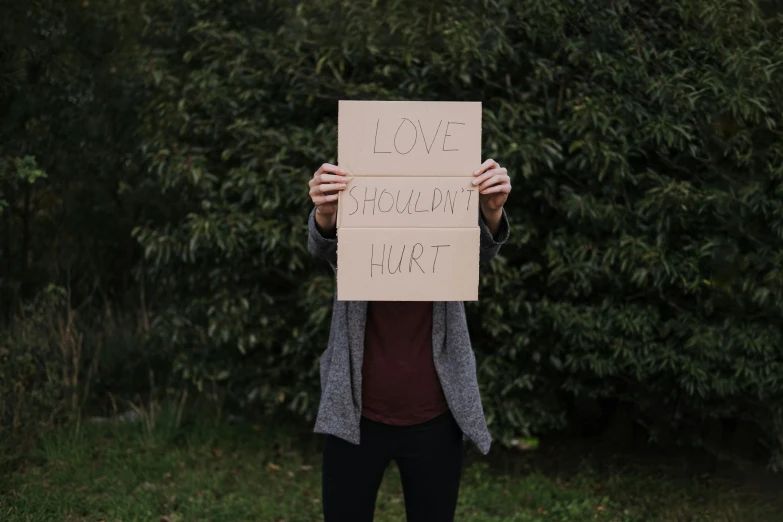 a woman holding a sign in front of her face, trending on pexels, hurufiyya, broken heart, hugging his knees, profile image, shroud