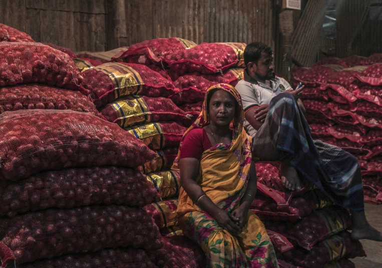 a couple of people sitting on top of a pile of onions, in a dark warehouse, tribals, on display, ultra - quality