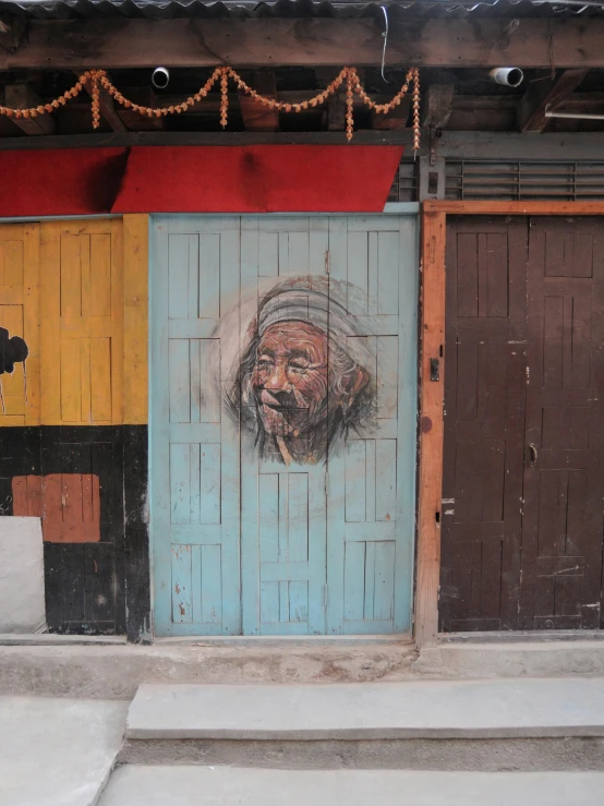 a painting of an old man on the side of a building, by Yi Insang, pexels contest winner, wood door, painted with pastels, nepal, in front of a garage